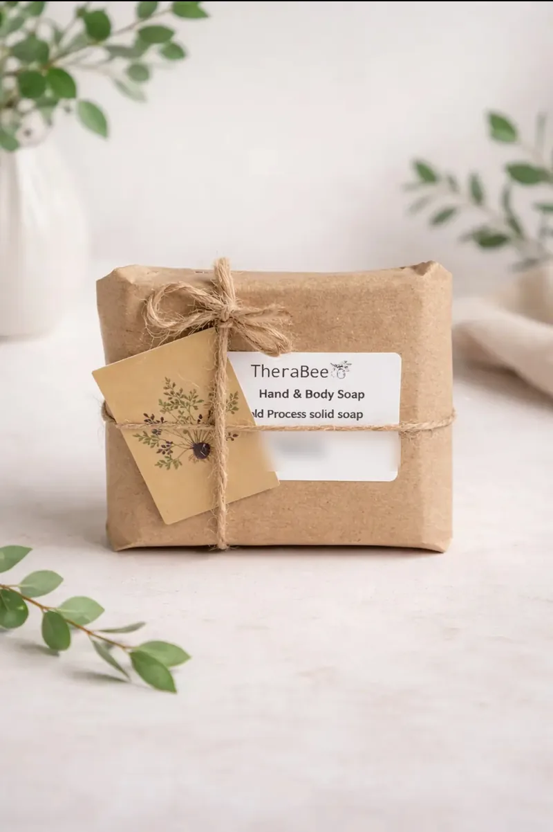 A bar of TheraBee soap wrapped in kraft paper, tied with jute twine, with a label and a small botanical tag